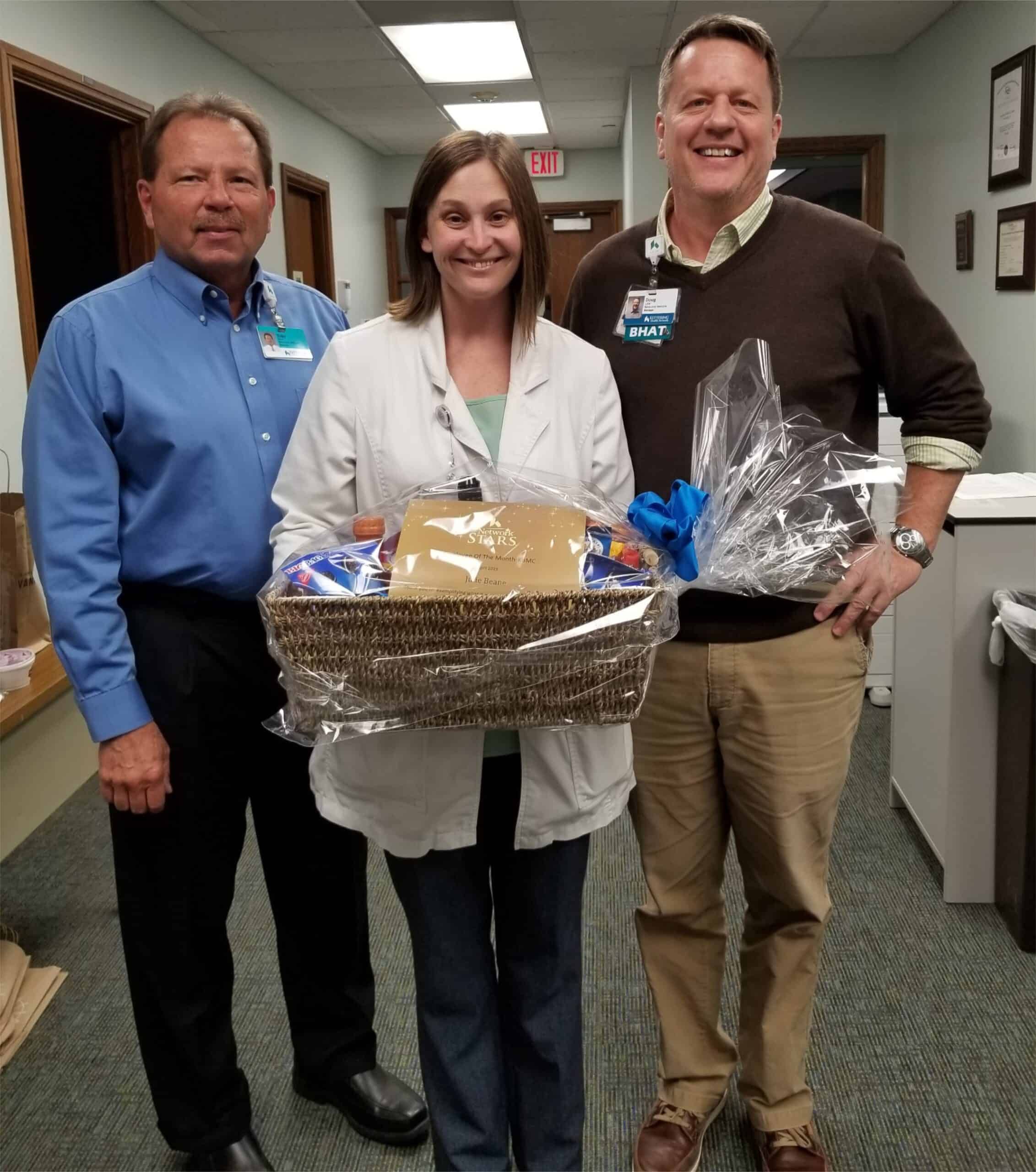 Three healthcare professionals presenting gift basket to employee recognition recipient