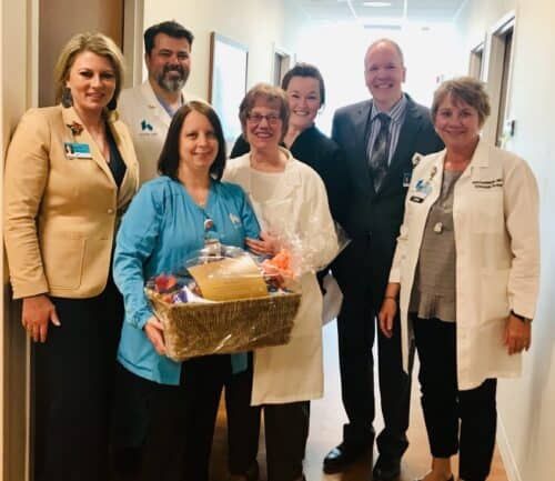 Healthcare staff presenting gift basket to patient in hospital hallway