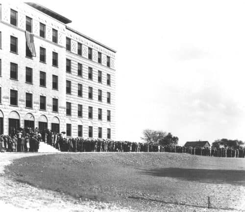 Historic black and white photograph showing crowds gathered outside a large institutional building.