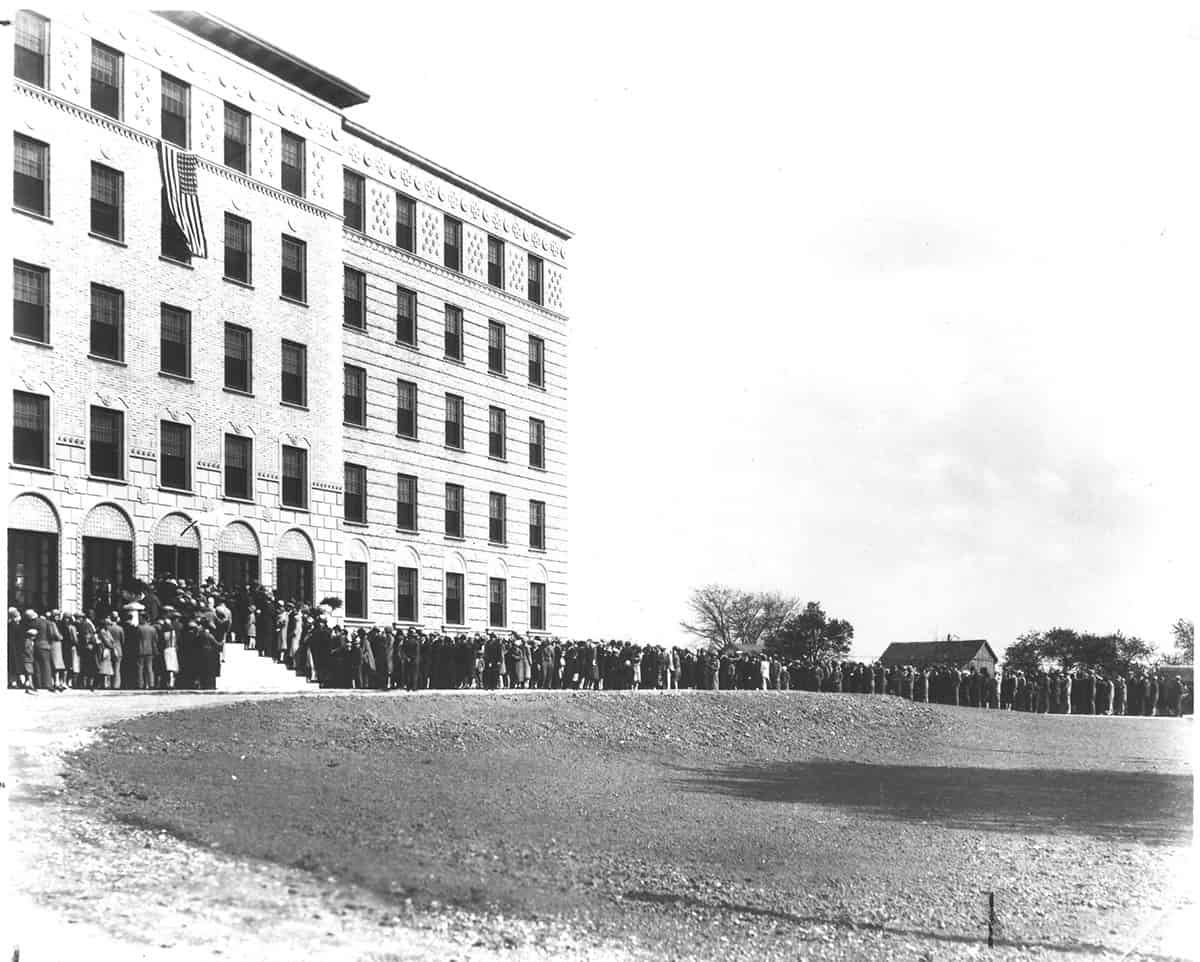 Historic black and white photograph showing crowds gathered outside a large institutional building.