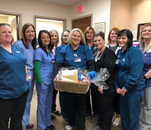 Healthcare team members gather around colleague holding gift basket in hospital hallway