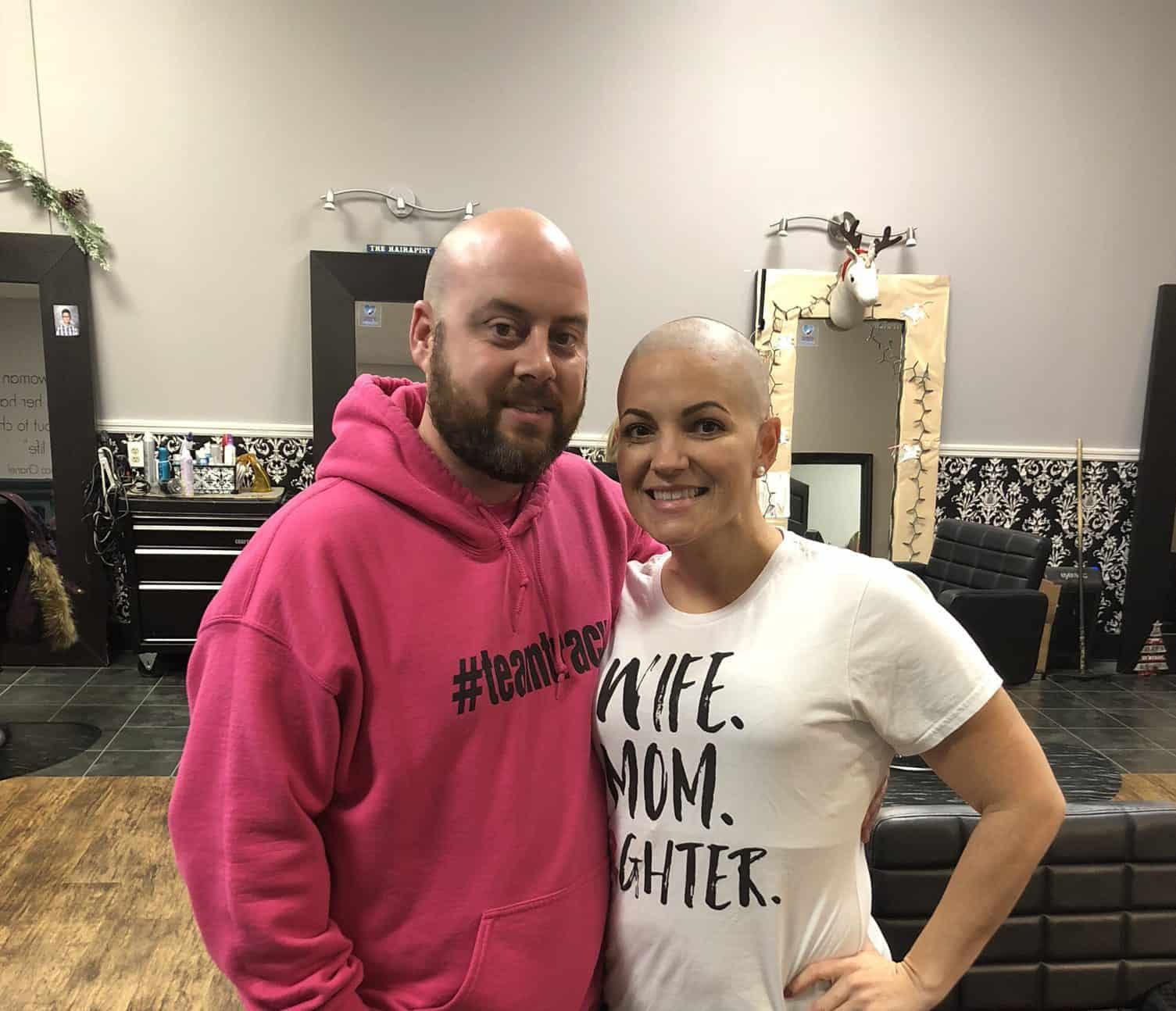 Couple embracing and smiling in salon, both with shaved heads showing solidarity