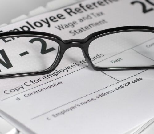 Black-rimmed glasses resting on W-2 tax form and employee reference documents