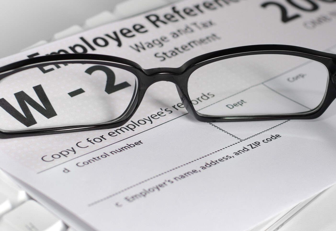 Black-rimmed glasses resting on W-2 tax form and employee reference documents