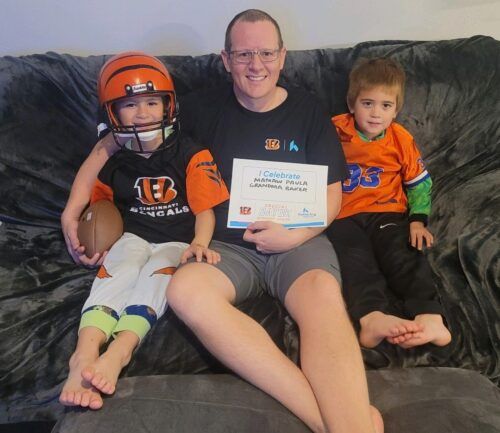 Adult with two children wearing Cincinnati Bengals gear sitting on couch holding celebration certificate