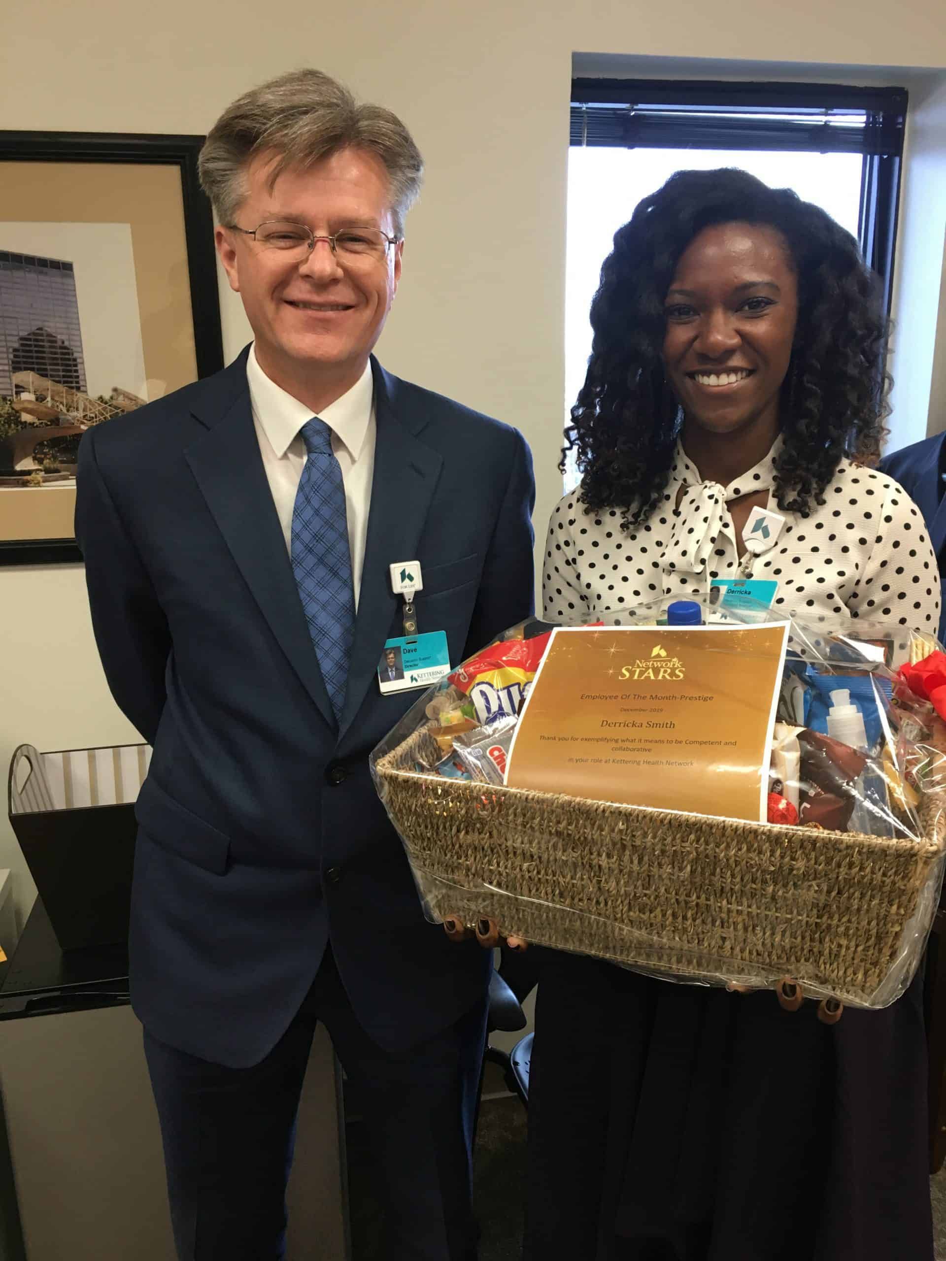 Man in suit presenting gift basket to woman in polka dot shirt