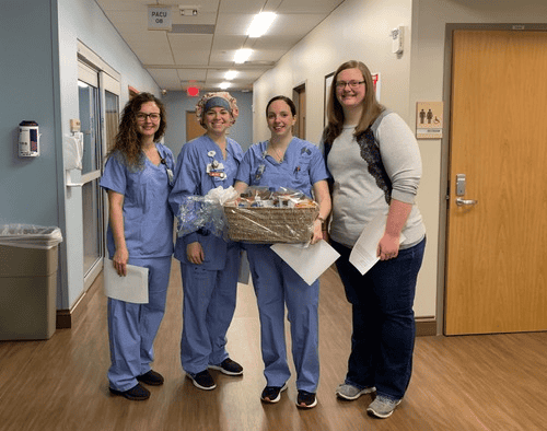 Four healthcare workers in scrubs posing together with gift basket in hospital hallway