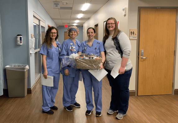 Four healthcare workers in scrubs posing together with gift basket in hospital hallway