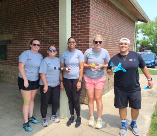 Five female healthcare workers in athletic wear posing together outdoors holding fitness equipment