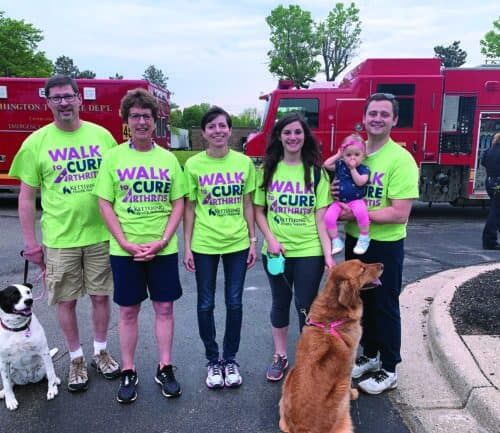 Five people in bright green "Walk to Cure Arthritis" t-shirts posing with dogs and baby.