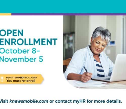 Woman with gray hair writing while looking at laptop during open enrollment period