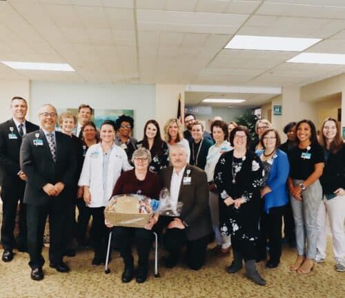 Healthcare team gathering in hospital lobby presenting gift basket to seated colleagues