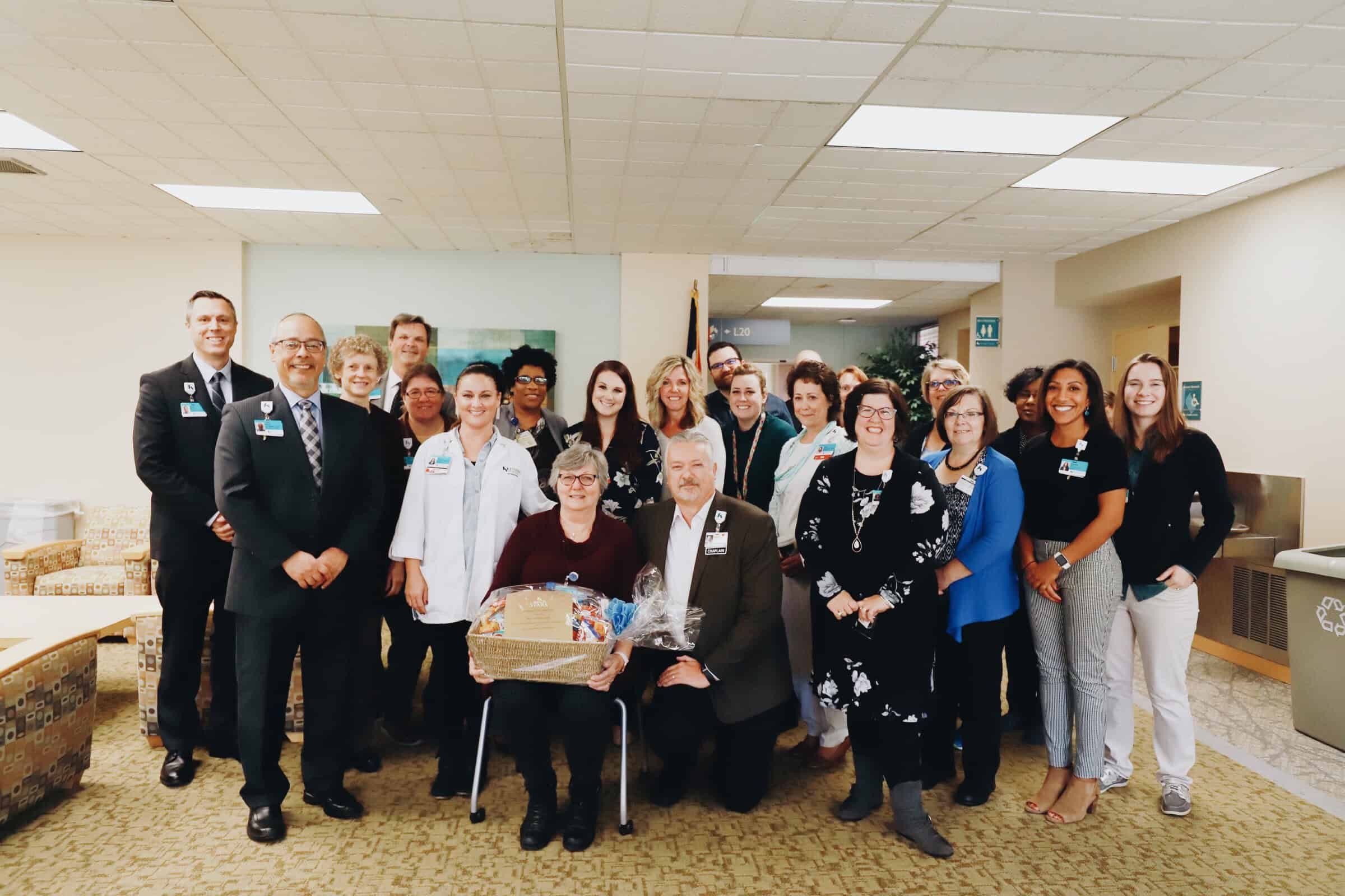 Healthcare team gathering in hospital lobby presenting gift basket to seated colleagues