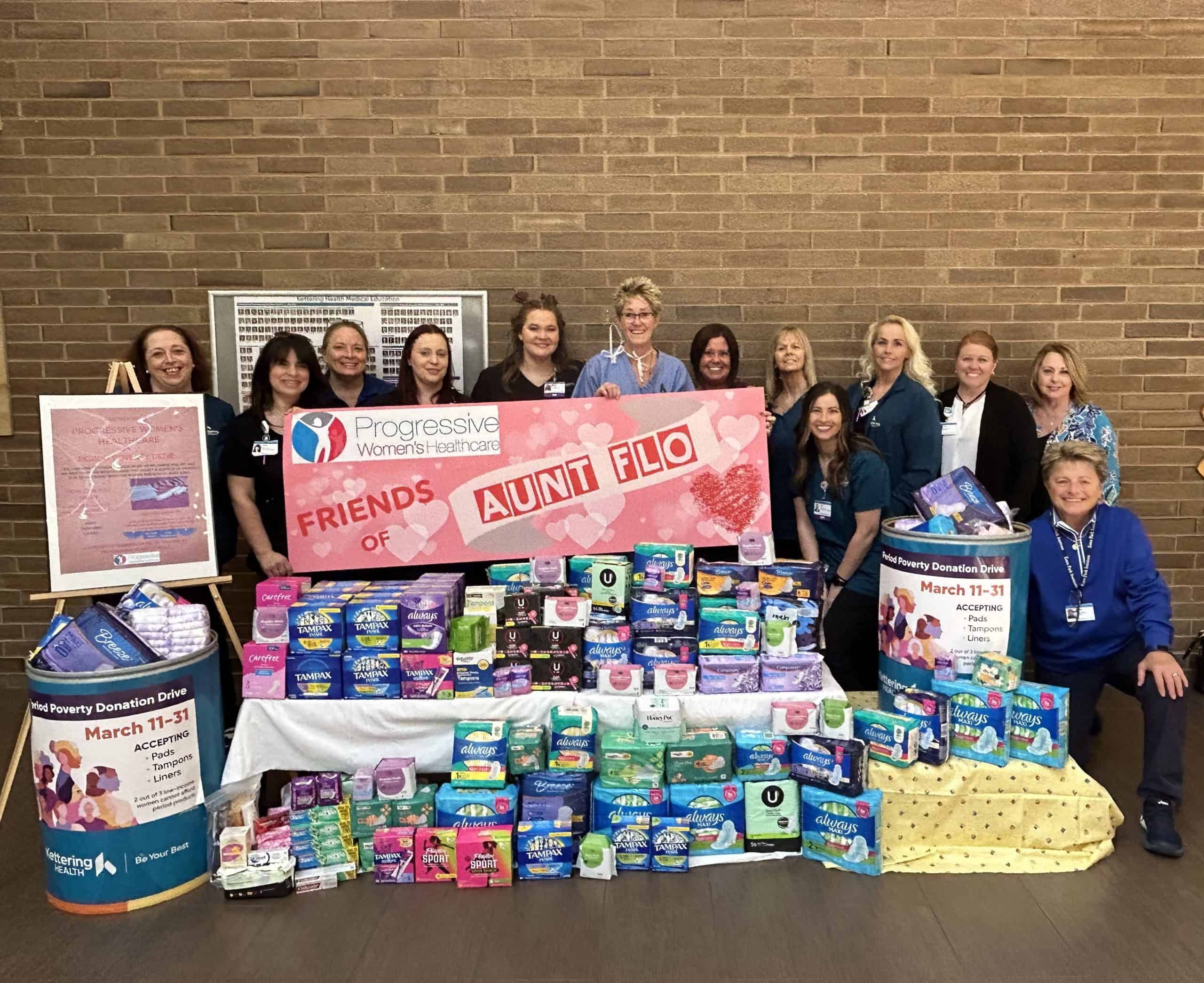 Healthcare workers standing behind table displaying donated feminine hygiene products for charity drive