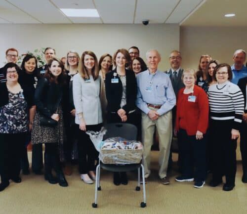 Large group of healthcare staff members posing together in hospital hallway with gift basket