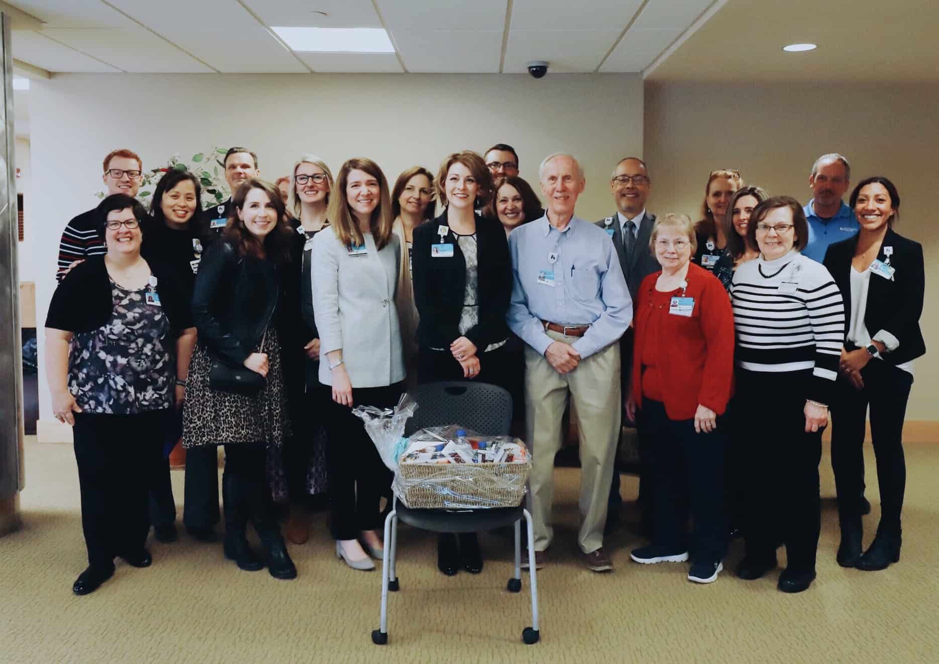 Large group of healthcare staff members posing together in hospital hallway with gift basket
