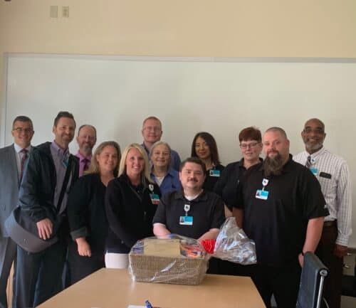 Group of healthcare staff members posing together around gift basket in conference room