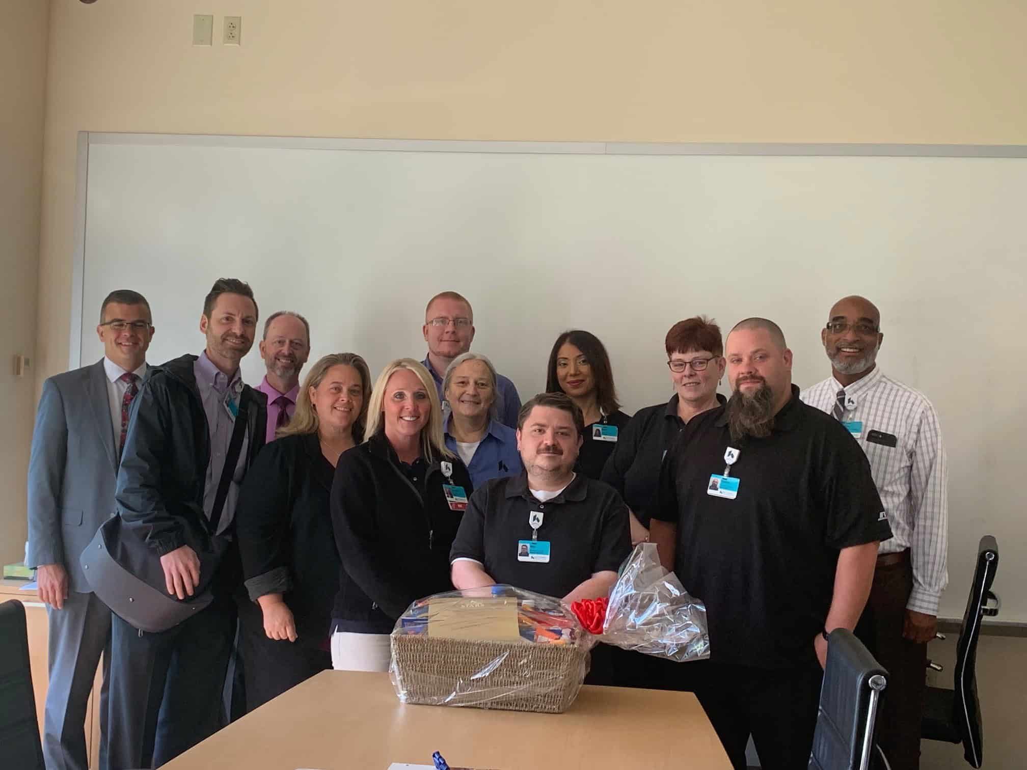 Group of healthcare staff members posing together around gift basket in conference room
