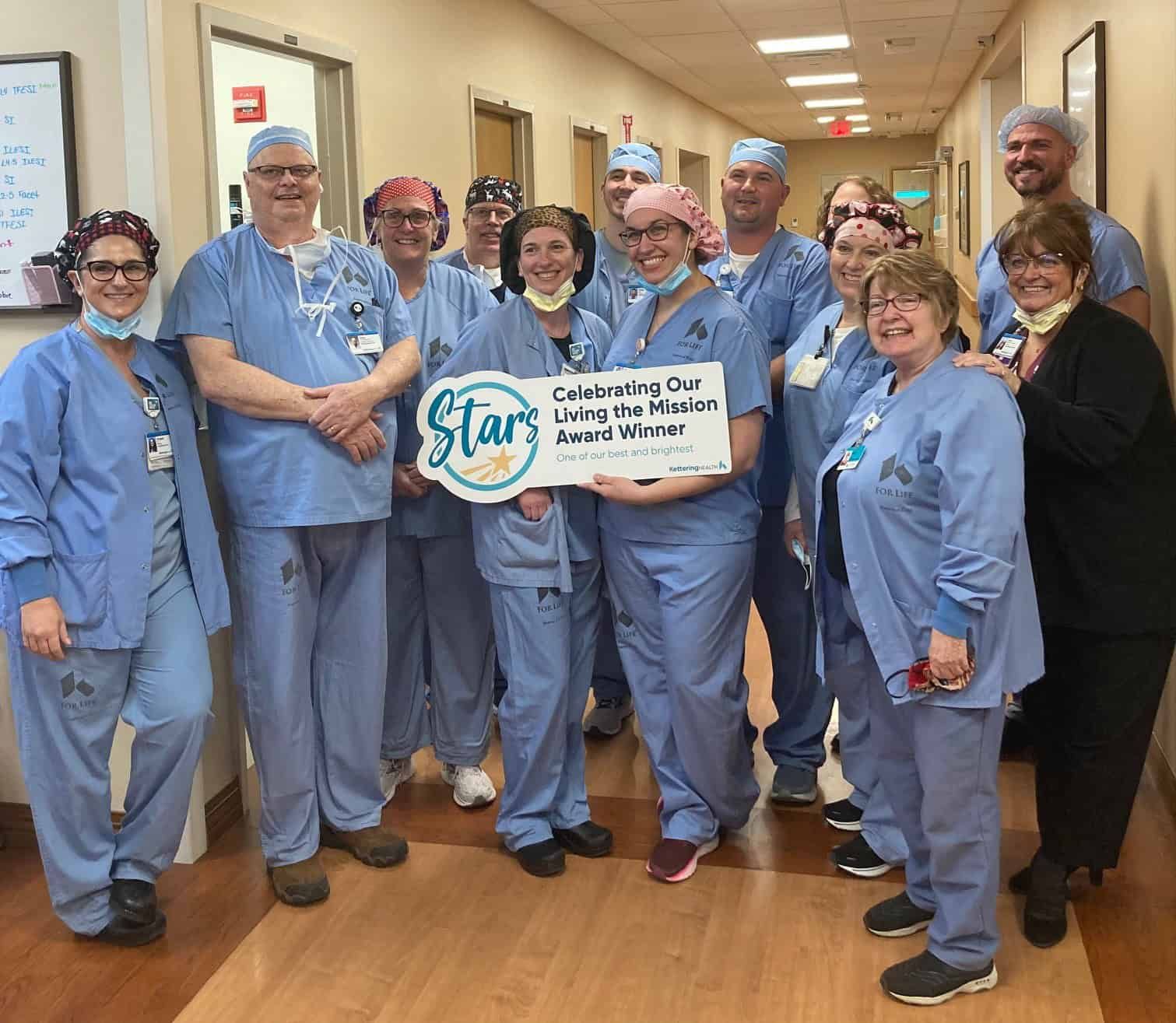 Medical team in blue scrubs celebrating with "Living the Mission Award Winner" banner