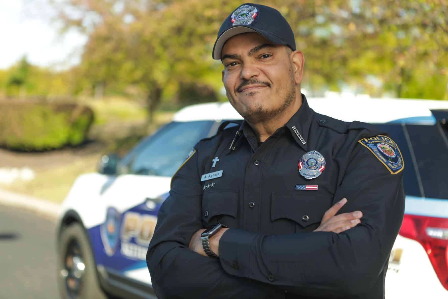 Smiling police officer in uniform with arms crossed standing beside patrol car