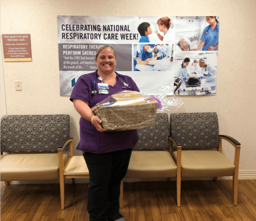 Healthcare worker in purple scrubs holding gift basket in hospital waiting area