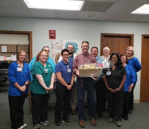 Group of healthcare staff presenting gift basket to colleague in hospital setting