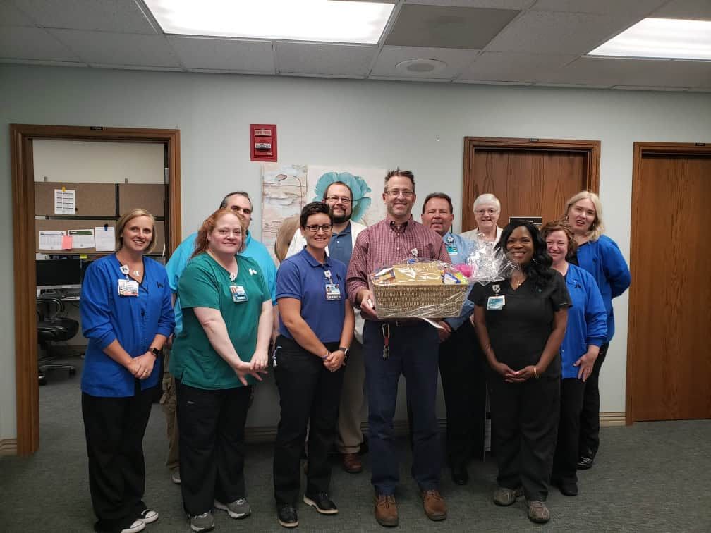 Group of healthcare staff presenting gift basket to colleague in hospital setting