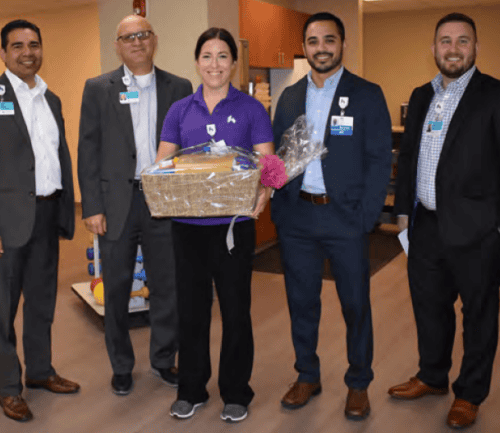 Five healthcare professionals standing together, woman in center holding gift basket and flowers