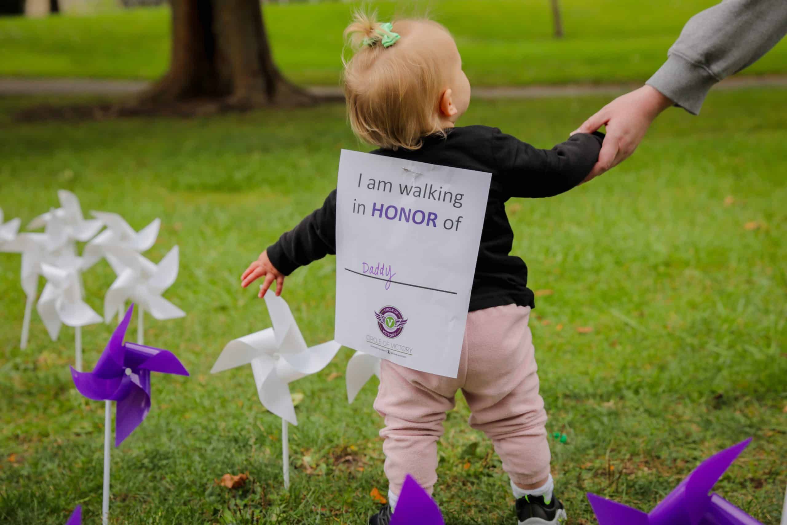 Young child walking with adult holding sign reading "I am walking in HONOR of Daddy"