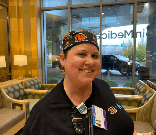 Healthcare worker in Cincinnati Bengals cap sitting in hospital lobby smiling at camera