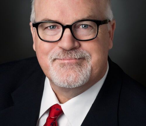 Professional headshot of Terry Burns wearing dark suit, red tie, and glasses