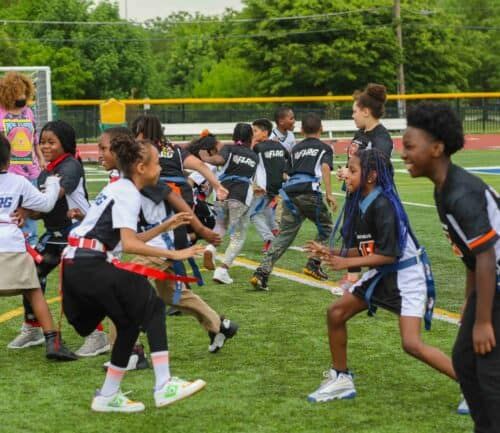 Children playing flag football on a grassy field during an outdoor sports event.