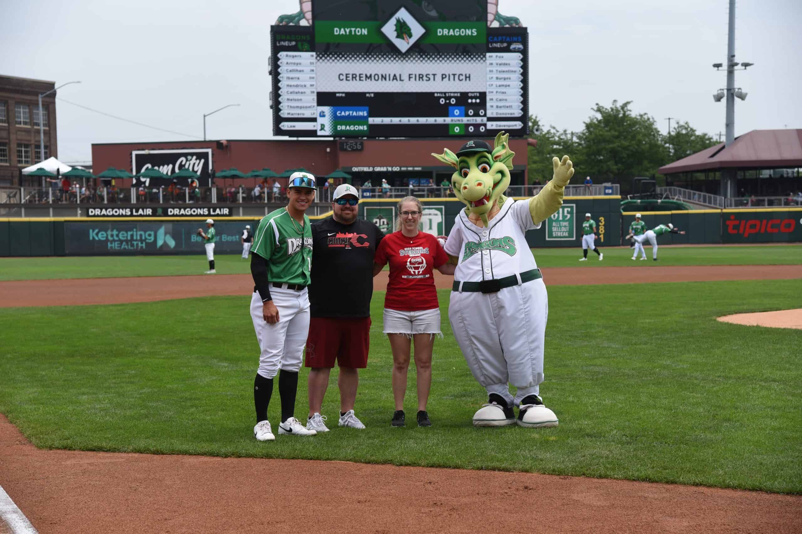 Four people posing on baseball field with Dragons mascot during ceremonial first pitch
