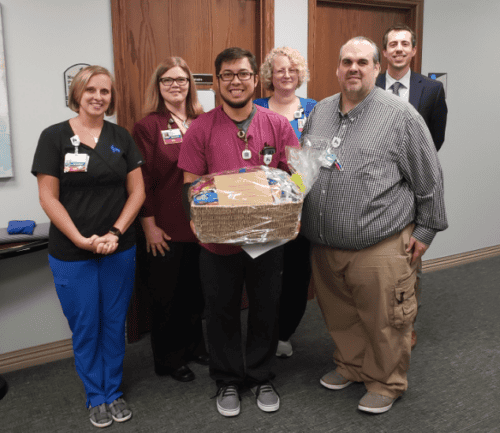 Healthcare team members presenting gift basket to colleague in hospital hallway