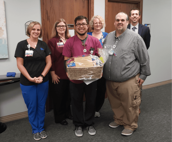 Healthcare team members presenting gift basket to colleague in hospital hallway