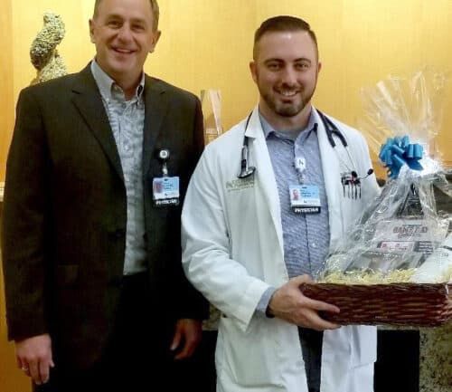 Two healthcare professionals posing together, one holding a gift basket in medical facility