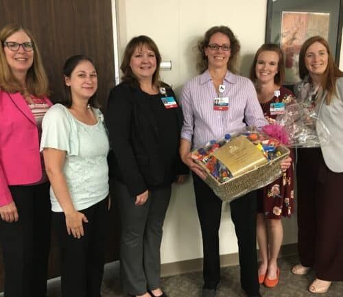 Six healthcare professionals posing together, one holding a large gift basket with chocolates and treats.