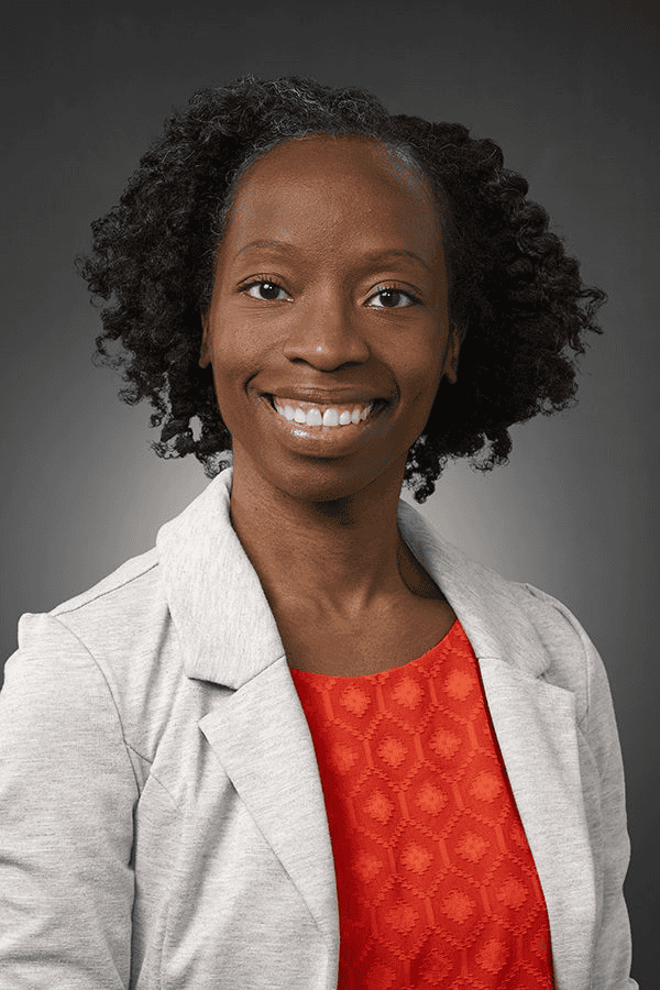 Professional headshot of Chioma Lindo wearing gray blazer and red top, smiling warmly