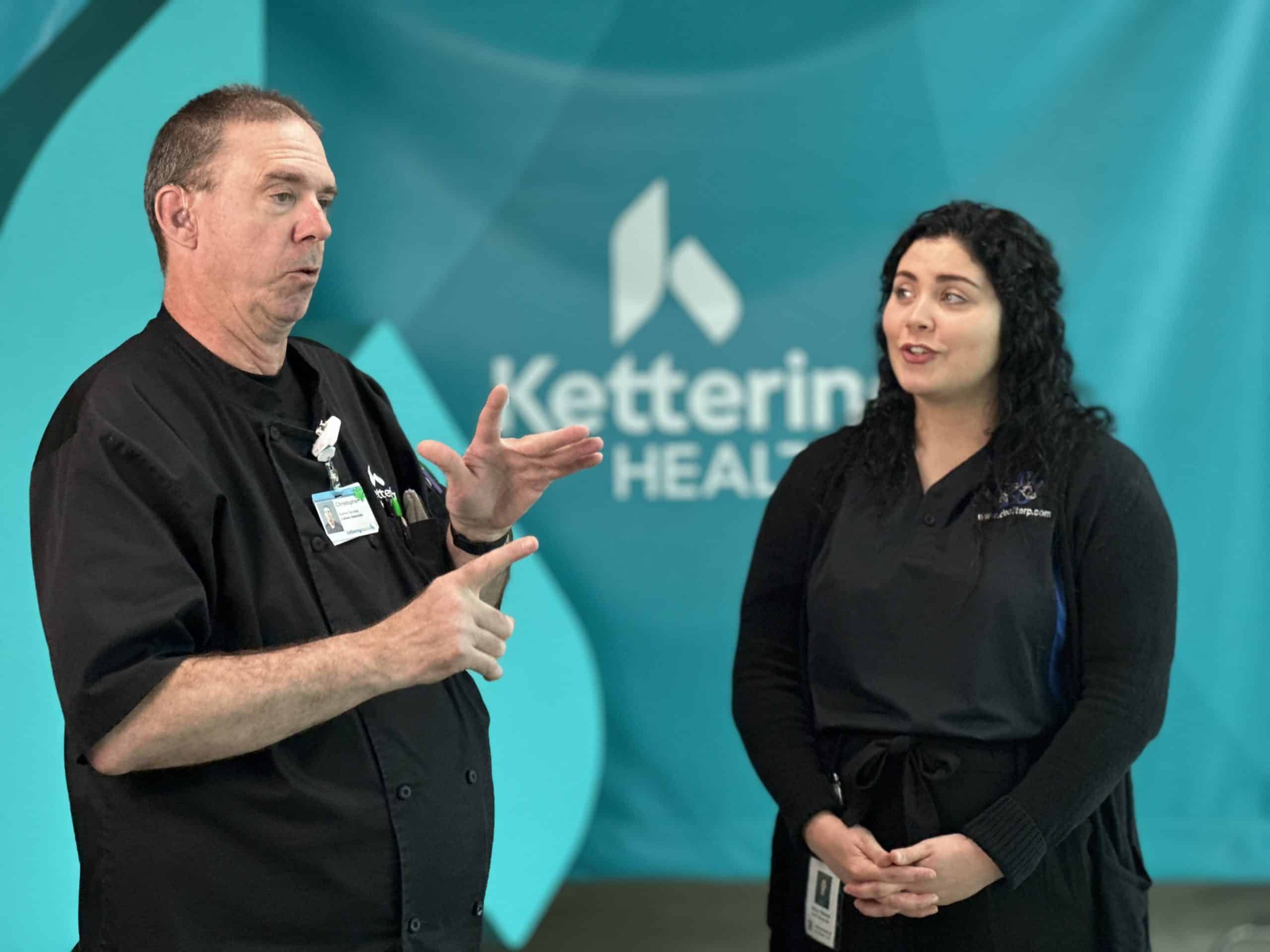 Two healthcare professionals in black uniforms discussing work at Kettering Health facility