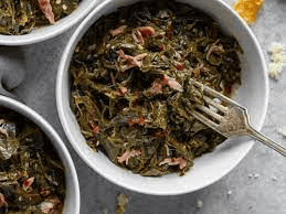 Bowl of cooked collard greens with serving spoon on white table
