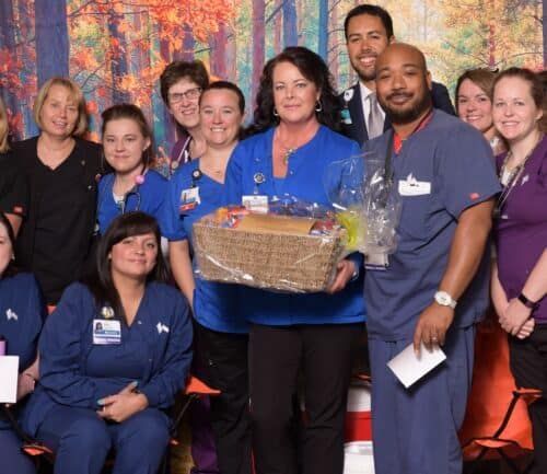 Healthcare team members posing together, with one person holding a gift basket in center