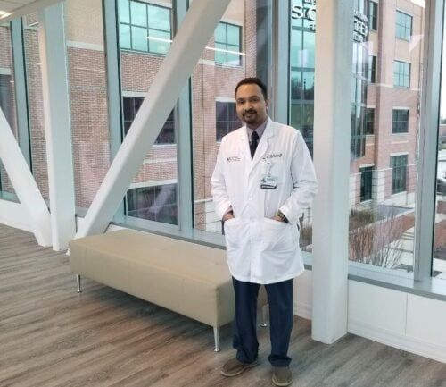 Doctor in white coat standing in modern hospital lobby with large windows