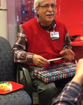 Doctor in red vest and glasses reading to patients in healthcare waiting area