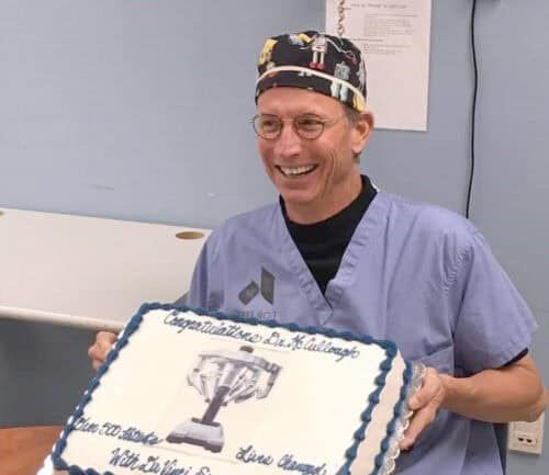 Doctor in scrubs holding congratulatory cake celebrating milestone achievement at Kettering Health