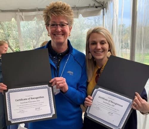 Two healthcare professionals holding certificates of recognition at award ceremony