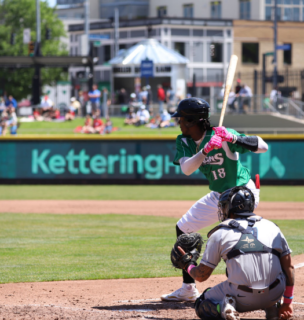 Baseball player in green jersey swinging bat at Kettering Health sponsored stadium