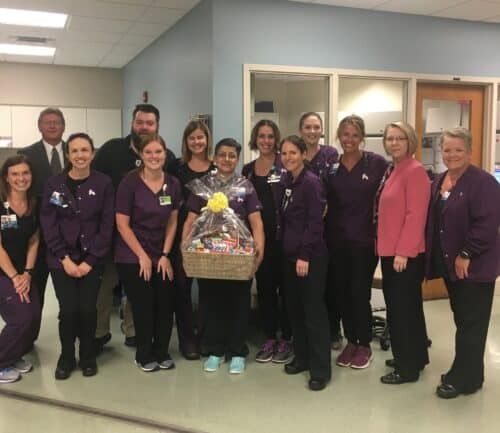 Healthcare staff in purple scrubs posing together with gift basket in hospital hallway