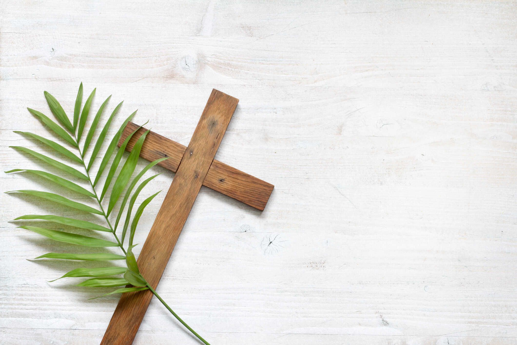 Wooden cross with green palm frond on white weathered background for Easter
