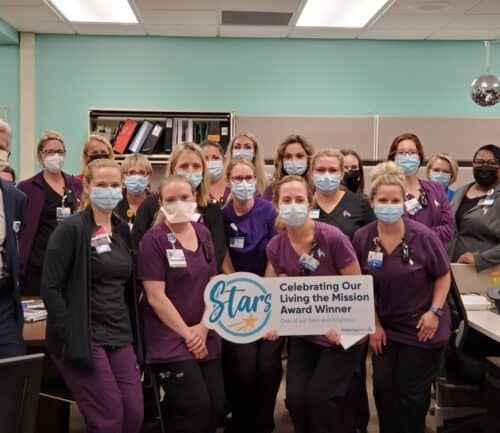 Healthcare team celebrating Living the Mission Award Winner with ceremonial banner