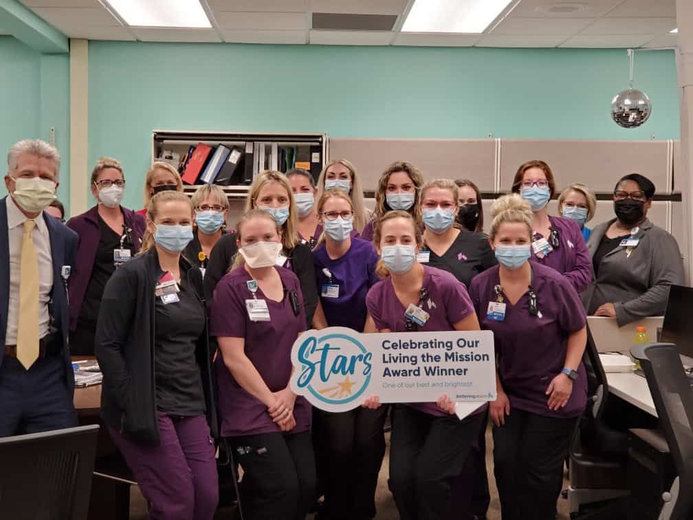 Healthcare team celebrating Living the Mission Award Winner with ceremonial banner